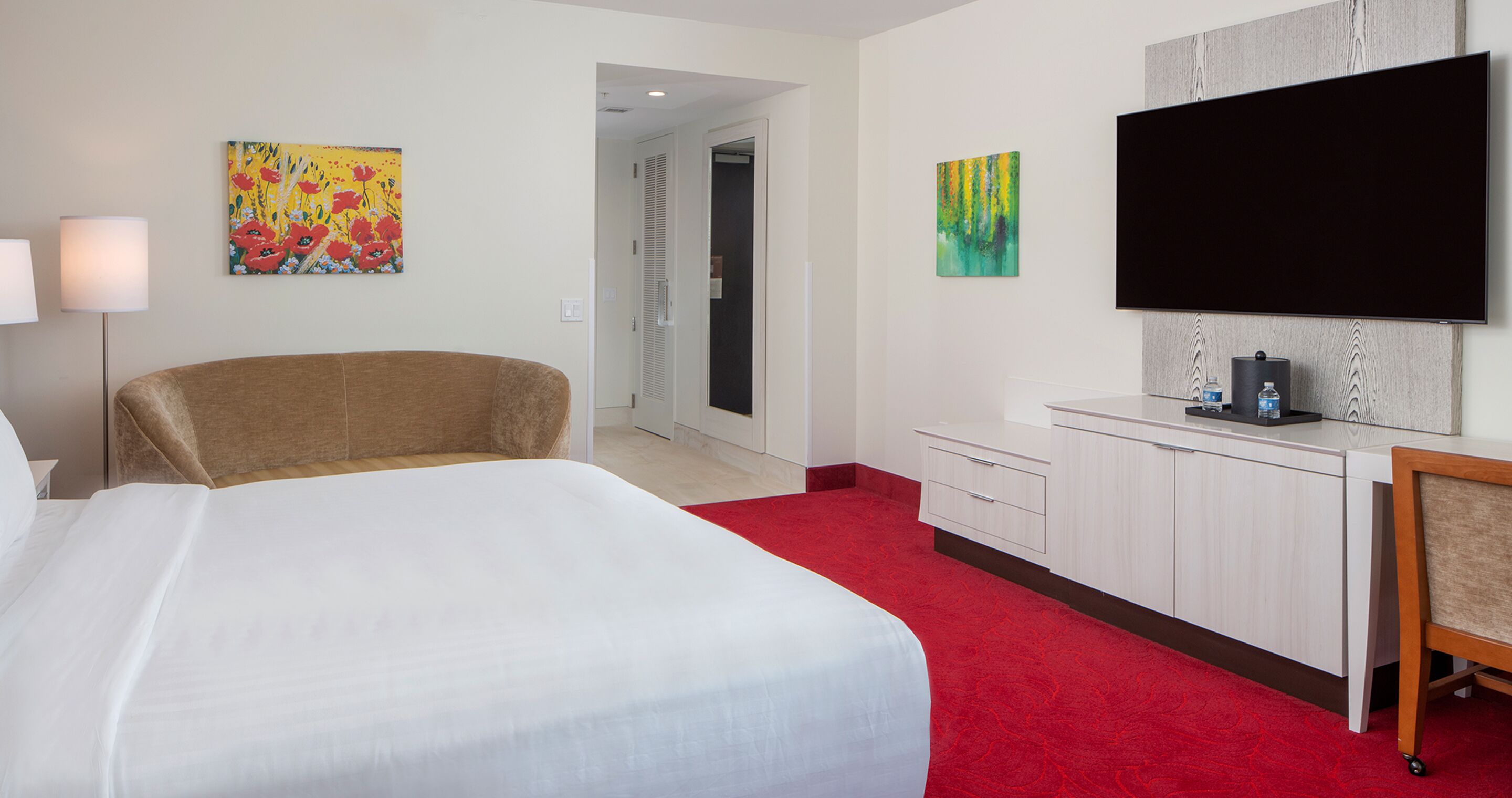A hotel room with a bed, a desk, a television, and artwork on the walls.