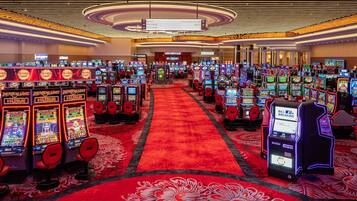 A casino with multiple slot machines arranged in rows, a red carpet, and directional signs for the buffet, lucky north club, and restroom.