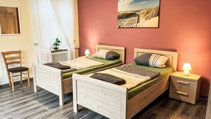 Ett rum med två sängar av trä, ett skrivbord, en stol, ett element och en tavla på väggen.