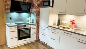 Ett modernt kök med vita skåp, en tegelvägg, en mikrovågsugn, en Samsung-ugn och ett trägolv.
