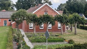Ett hus byggt av rött tegel med ett triangulärt tak, omgivet av välskötta trädgårdar och träd.