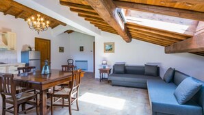 Un'ampia zona giorno con tavolo da pranzo, travi in legno al soffitto e un divano grigio.