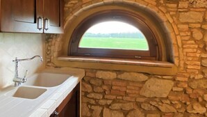 Une cuisine avec un mur en pierre, une fenêtre donnant sur un champ verdoyant et des armoires en bois.