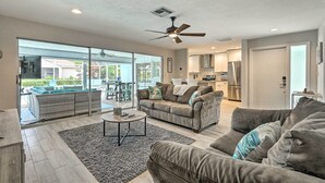 A spacious living room with a large gray sectional sofa, a coffee table, and a ceiling fan. A sliding glass door leads to a patio with outdoor furniture. - Bright & Breezy Cape Coral Retreat w/ Pool! (Cape Coral)