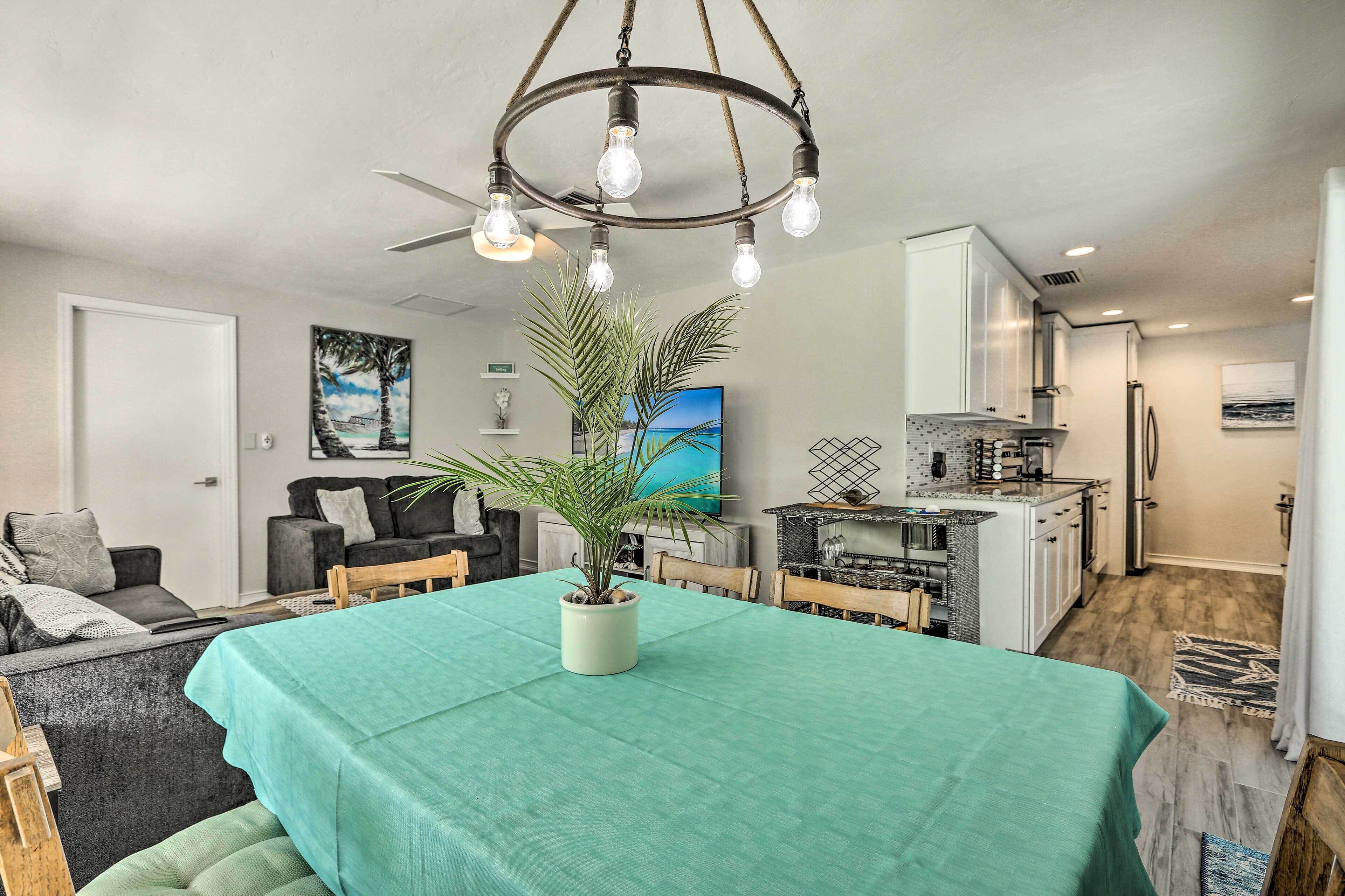 Un coin repas avec une table dressée pour quatre personnes, un ventilateur de plafond et une cuisine en arrière-plan.