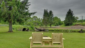 A wooden bench with a table in a grassy area with a pond and trees in the background. - Quiet Country Escape: Fire Pit, Fish On-Site! (West Edmeston)