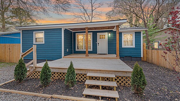 Una casa de dos pisos con fachada azul, un porche con escalones y una valla de madera.