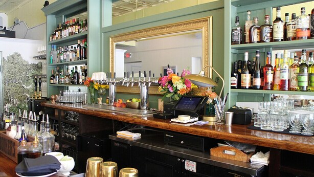 A bar area with a cash register, bar tools, and a variety of liquor bottles. - Contemporary 3-Bedroom Home with Balcony in RVA (Richmond)