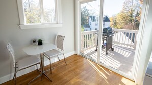 A room with a white table and two chairs, a window, and a sliding glass door leading to a deck with a barbecue grill. - Contemporary 3-Bedroom Home with Balcony in RVA (Richmond)