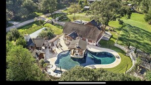 An aerial view of a large property with a swimming pool, multiple buildings, and well-maintained lawns.