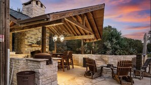 An outdoor patio with stone walls, wooden furniture, and a stone fireplace.
