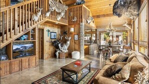 A spacious living room with wooden walls and ceiling, a large TV, a sofa, and various animal taxidermy.
