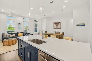 Une cuisine moderne dotée d’un grand îlot central, d’appareils électroménagers en acier inoxydable et de luminaires suspendus.
