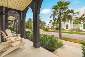 Un espace extérieur aménagé avec des sièges sous une pergola, des fauteuils Adirondack, un palmier et une vue sur la rue.