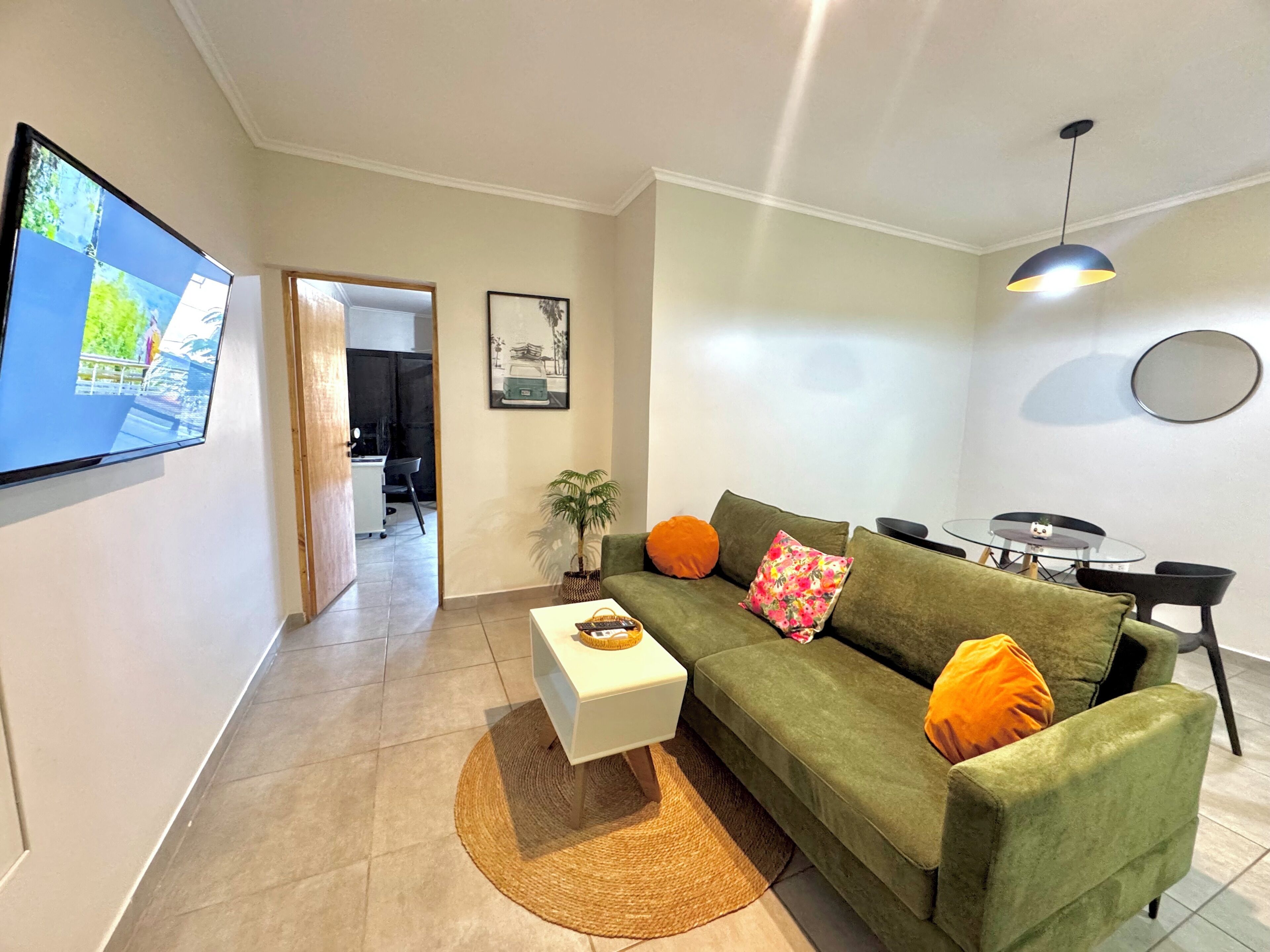 A living room with a green sofa, a white coffee table, and a TV mounted on the wall.