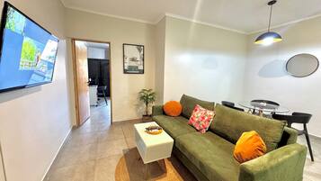 A living room with a green sofa, a white coffee table, and a TV mounted on the wall.