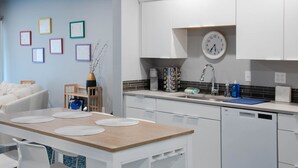 Una cocina moderna con armarios blancos, una mesa de comedor de madera con individuales, un reloj y un jarrón con ramas.