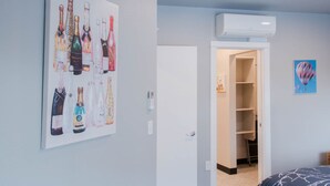 Una habitación con una obra de arte colgada en la pared que muestra botellas de champán, una puerta blanca, un equipo de aire acondicionado y un cuadro con globos aerostáticos.
