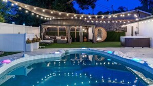 A backyard with a swimming pool, a covered seating area, and string lights. - Spacious Luxury 4 bdr, Pool, Hot Tub, Sauna, Patio (Los Angeles)