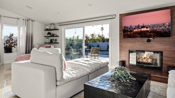 A modern living room with a white sofa, a coffee table, a fireplace, and a TV mounted on the wall. - Spacious Luxury 4 bdr, Pool, Hot Tub, Sauna, Patio (Los Angeles)