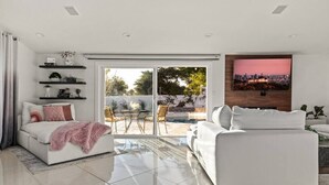 A modern living room with a white sofa, a white armchair, and a glass door leading to a patio with a pool. - Spacious Luxury 4 bdr, Pool, Hot Tub, Sauna, Patio (Los Angeles)