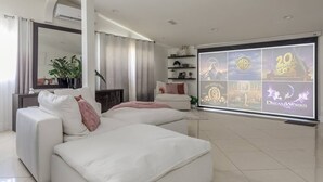 A modern living room with a white sofa, a large flat-screen TV displaying movie titles, and a minimalist decor. - Spacious Luxury 4 bdr, Pool, Hot Tub, Sauna, Patio (Los Angeles)