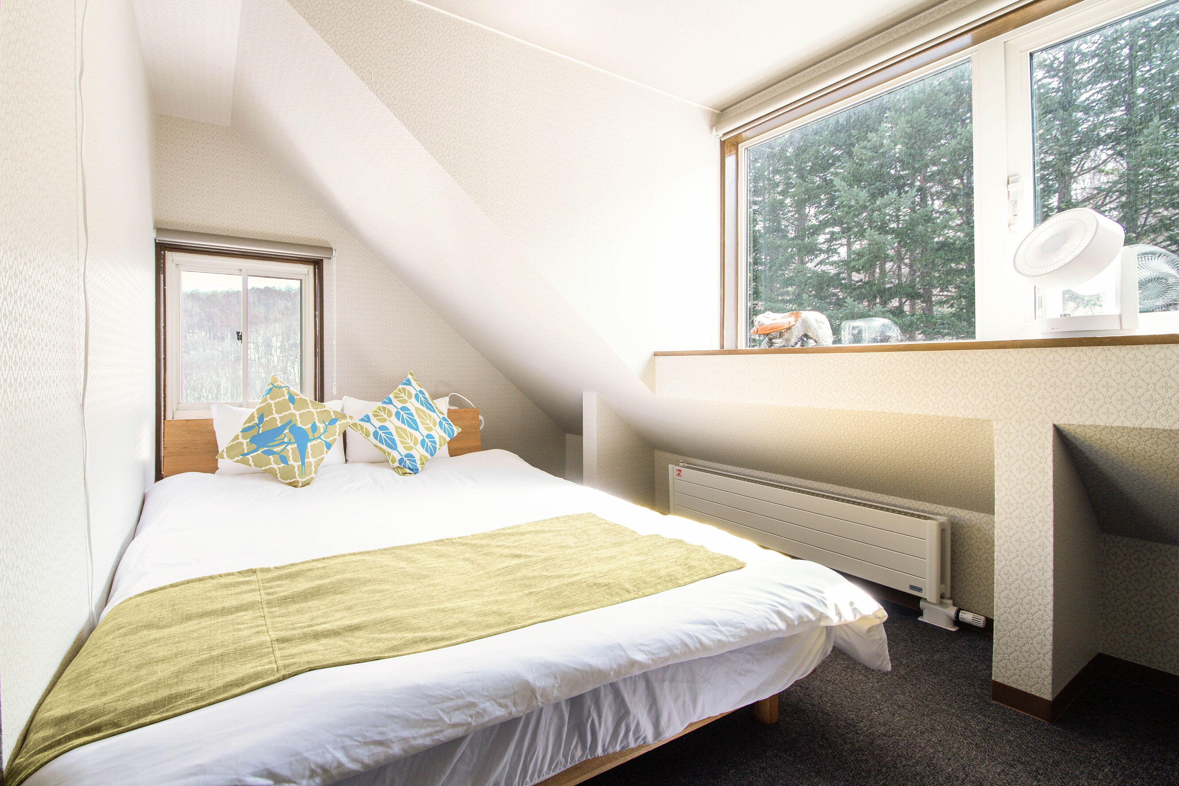 A bedroom with a bed, a window, a radiator, and a desk.