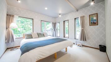 A spacious bedroom with a large bed, multiple windows, and a view of greenery outside.