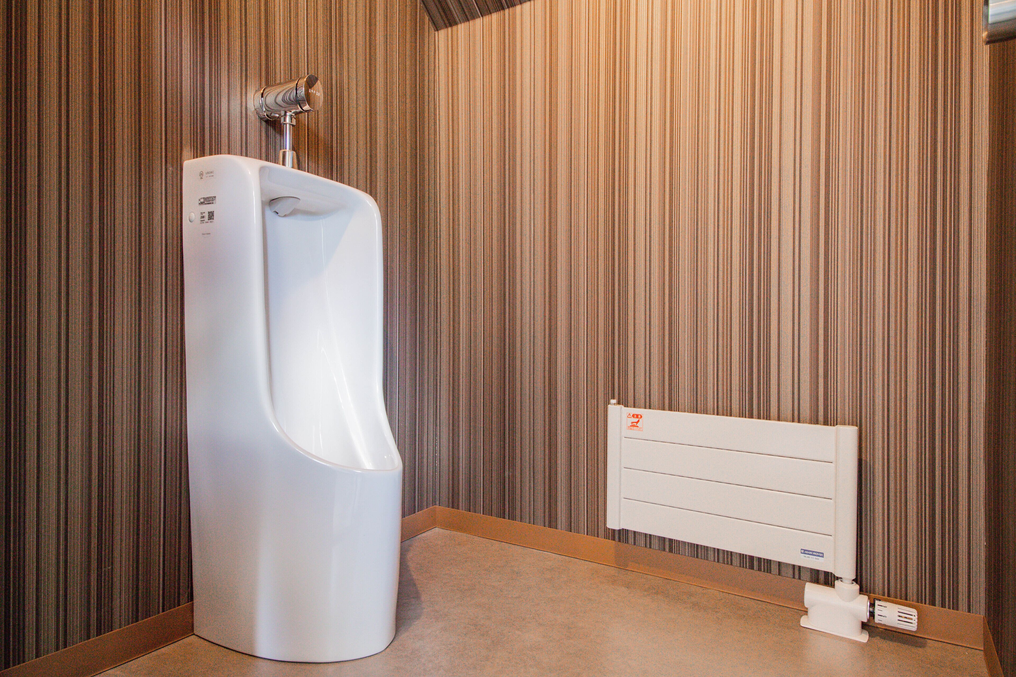 A urinal in a restroom with a striped wall and a radiator.