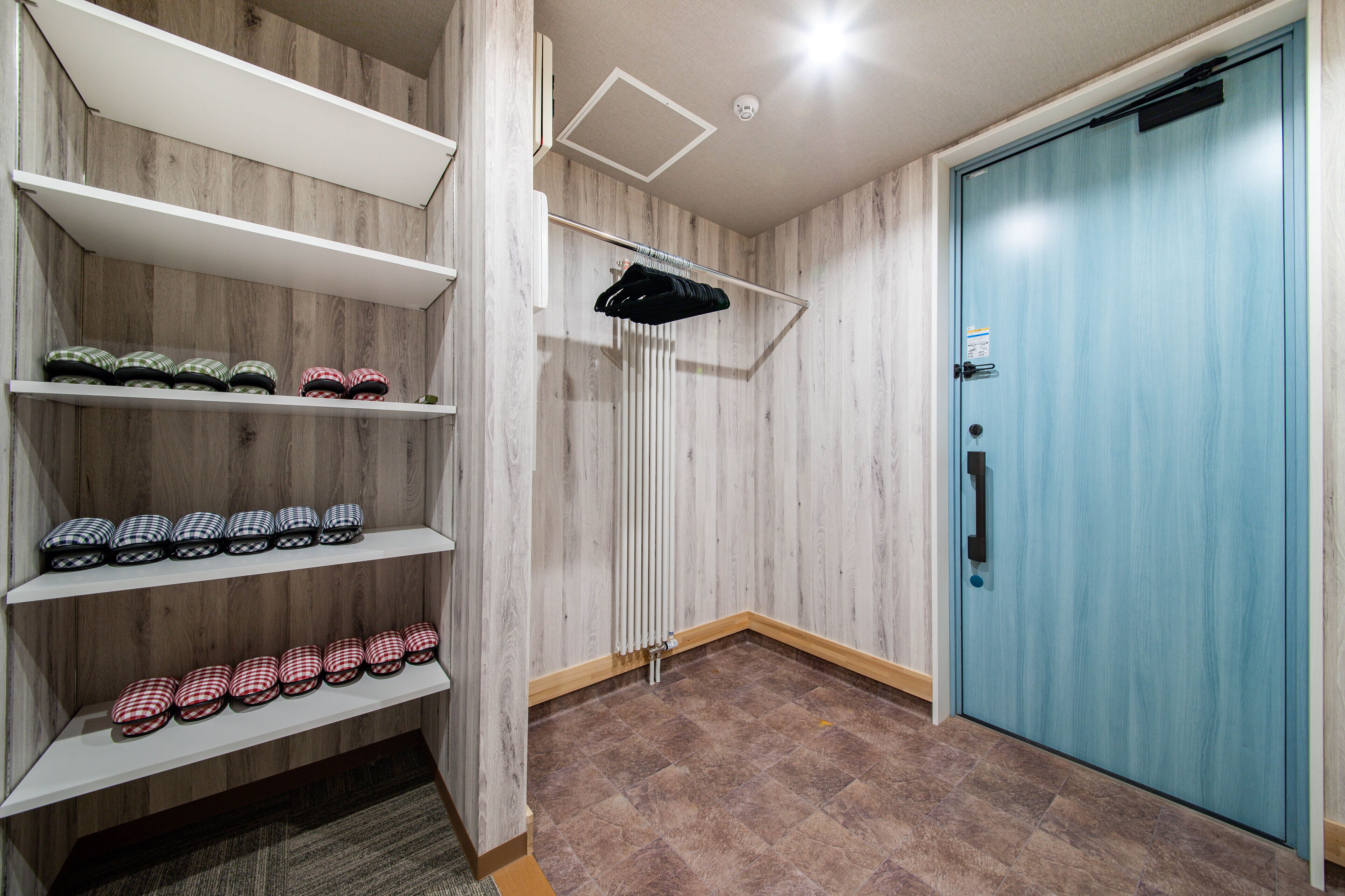 A room with wooden walls, a blue door, and shelves with shoes.