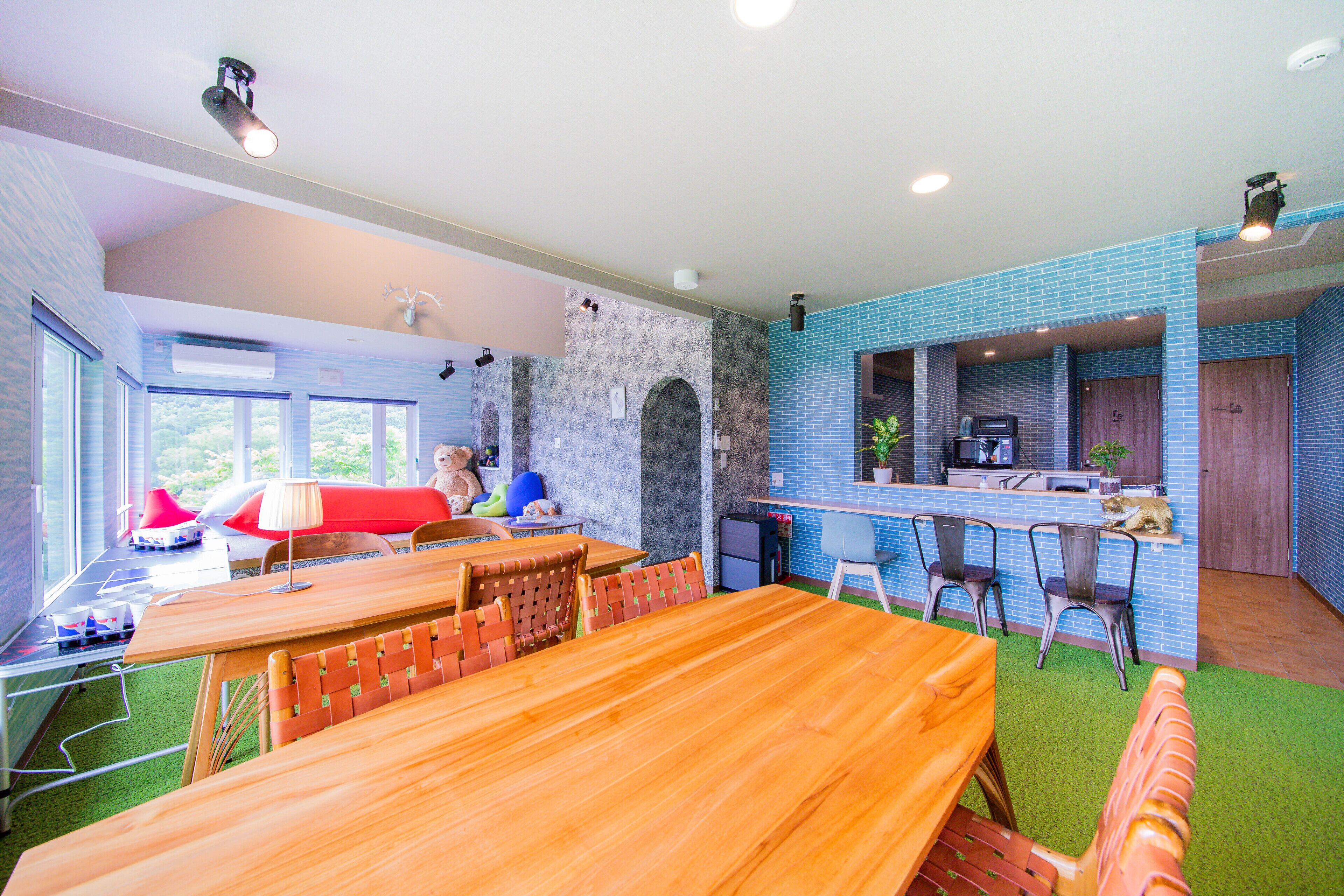 Un comedor amplio con una larga mesa de madera y sillas, una cocina con paredes de azulejos azules, y vistas al verdor exterior.