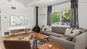A modern living room with a fireplace, a sofa, a coffee table, and a large window with curtains. - MCM Retreat w/ Pool & Spa | Lush, Quiet, Central (Spring Valley)