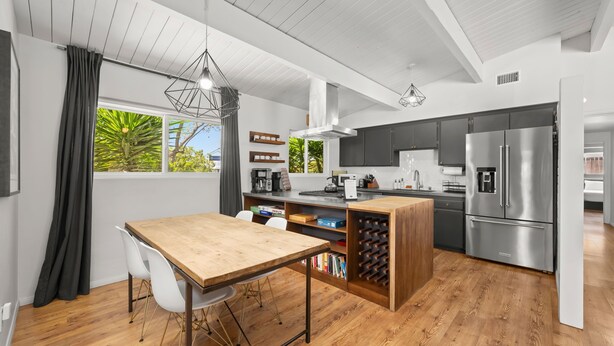 A modern kitchen with a wooden dining table, white chairs, a built-in wine rack, and a stainless steel refrigerator. - MCM Retreat w/ Pool & Spa | Lush, Quiet, Central (Spring Valley)