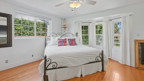 A bedroom with a large bed, white curtains, a ceiling fan, and a view of greenery outside. - Stylish San Fernando Stay with Designer Kitchen Upgrade (San Fernando)