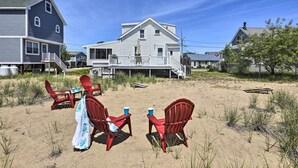 Ein Anwesen direkt am Strand mit einem großen Haus, einer überdachten Veranda mit roten Stühlen und einem Tisch sowie einer Sandstrandfläche.