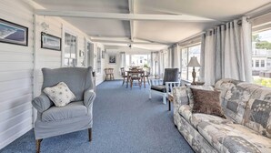 Eine überdachte Veranda mit Esstisch und Stühlen, einem grauen Sessel und einem gemusterten Sofa.