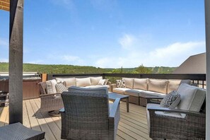 An outdoor deck with wicker furniture, a wooden table, and a view of the landscape.
