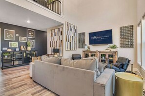 A modern living room with a grey sofa, a black leather chair, and a TV mounted on the wall. There is a decorative wall panel and a cabinet with glass doors.