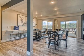 Un vaste espace dédié à la salle à manger, avec une longue table et de nombreuses chaises, de grandes fenêtres offrant une vue sur la verdure, et un plafond doté d’un éclairage encastré.