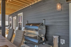 Ein Außenbereich mit Sitzgelegenheit, einem großen Grill, Korbmöbeln und einer Holzbeschichtung an der Decke.