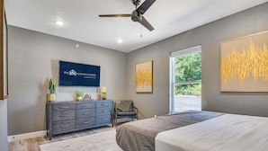 A bedroom with a bed, a dresser, a ceiling fan, and artwork on the walls.