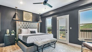 A bedroom with a large bed, a bench, a ceiling fan, and a view of the outdoors.