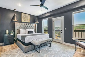 Une chambre avec un grand lit, un banc, un ventilateur de plafond et une vue sur l’extérieur.