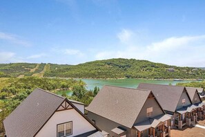 A row of modern, two-story houses with sloped roofs, set against a backdrop of a lake and green hills.