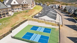 A tennis court with a surrounding fence, adjacent buildings, and a parking area.
