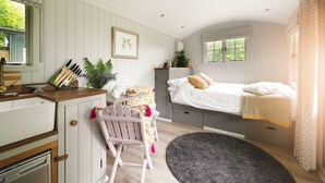 A cozy bedroom with a bed, a desk with a chair, a window with a view, and a small bathroom. - Red Deer Escape - Luxury Cottages (Minehead)
