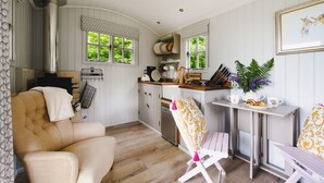 A cozy kitchen with wooden cabinets, a dining area with a table and chairs, and a window with a view of greenery. - Red Deer Escape - Luxury Cottages (Minehead)