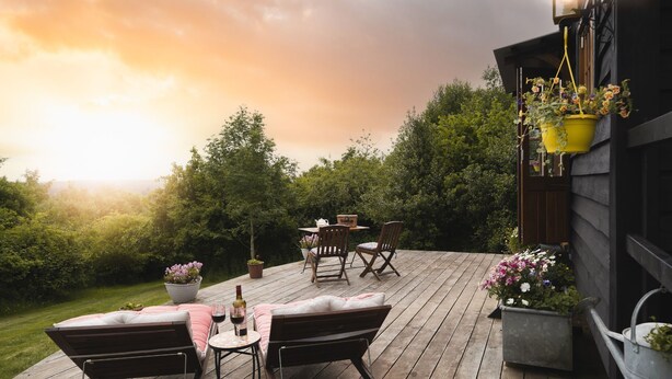A wooden deck with outdoor furniture, a table with a bottle and glasses, and potted plants. - Hooting Owl Retreat - Luxury Cottages (Minehead)