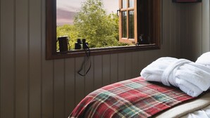 A bedroom with a large window, a plaid blanket, and a wooden headboard. - Hooting Owl Retreat - Luxury Cottages (Minehead)