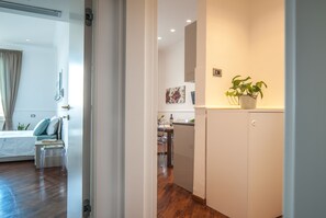 Une chambre d’hôtel moderne avec un plancher en bois, un lit, un bureau et un coin cuisine équipé d’un réfrigérateur et agrémenté d’une plante en pot.